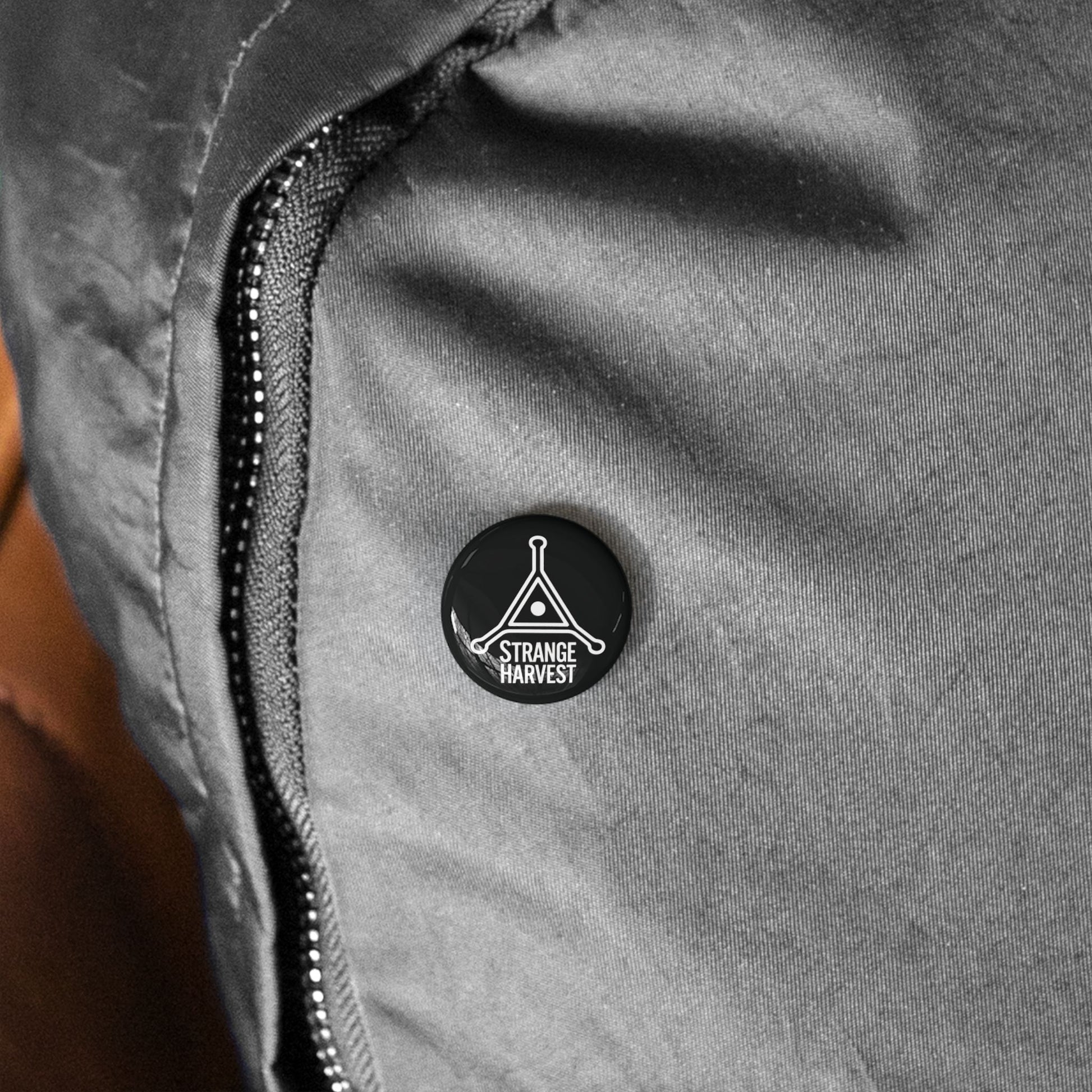 Close-up of a gray jacket with a black button featuring 'Strange Harvest' logo.