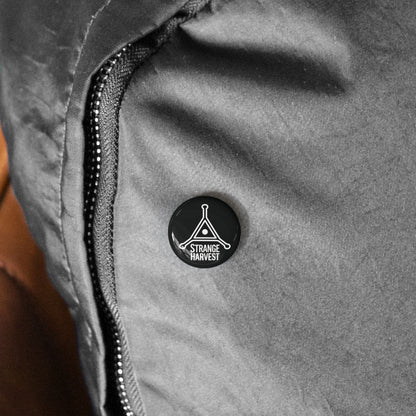 Close-up of a gray jacket with a black button featuring 'Strange Harvest' logo.