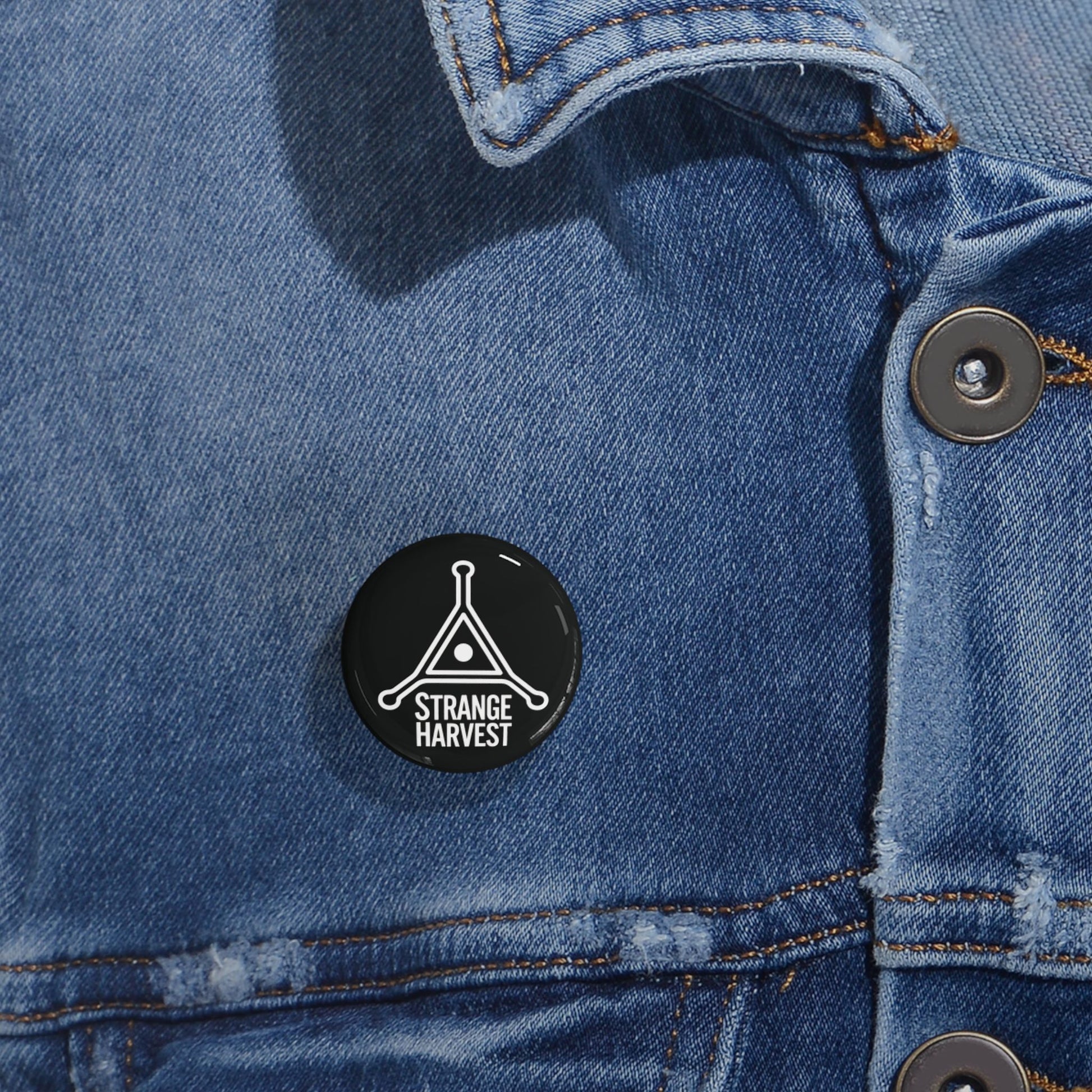 Black 'Strange Harvest' pin on a blue denim jacket